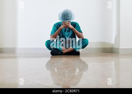 Weinende gestresste und müde Krankenschwester, die nach einem langen Arbeitstag auf dem Boden der Krankenhaushalle sitzt Stockfoto