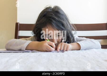 Grundschülerin macht ihre Hausaufgaben. Sie macht ihre eigenen Hausaufgaben allein zu Hause, weil die Schulen wegen der Corona pandemi geschlossen sind Stockfoto