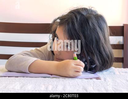 Grundschülerin macht ihre Hausaufgaben. Sie macht ihre eigenen Hausaufgaben allein zu Hause, weil die Schulen wegen der Corona pandemi geschlossen sind Stockfoto