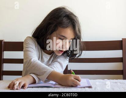 Grundschülerin macht ihre Hausaufgaben. Sie macht ihre eigenen Hausaufgaben allein zu Hause, weil die Schulen wegen der Corona pandemi geschlossen sind Stockfoto