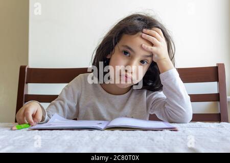 Grundschülerin macht ihre Hausaufgaben. Sie macht ihre eigenen Hausaufgaben allein zu Hause, weil die Schulen wegen der Corona pandemi geschlossen sind Stockfoto