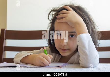 Grundschülerin macht ihre Hausaufgaben. Sie macht ihre eigenen Hausaufgaben allein zu Hause, weil die Schulen wegen der Corona pandemi geschlossen sind Stockfoto