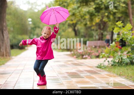 Kind Mädchen 2-3 Jahre alt zu Fuß auf Pfütze im Park mit rosa Regenschirm tragen wasserdichte Stiefel im Freien. Kindheit. Herbstsaison. Stockfoto