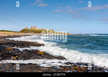 Wellen brechen auf den schwarzen Felsen von Dunstanburgh Castle, Northumberland, England Stockfoto
