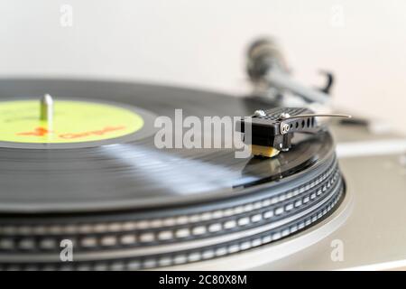Nahaufnahme eines Plattendecks mit S-förmigem Tonarm mit Stylus, der LP-Vinyl-Schallplatte auf Bandantrieb-Plattenspieler spielt. Bewegungsunschärfe. Einfacher Hintergrund. Stockfoto