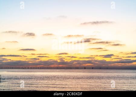 Der Morgenhimmel über dem Thanet Offshore Windpark vor der kent Coast bei Broadstairs. Wolken am Horizont mit orange-gelben Himmel über einem ruhigen Meer. Stockfoto