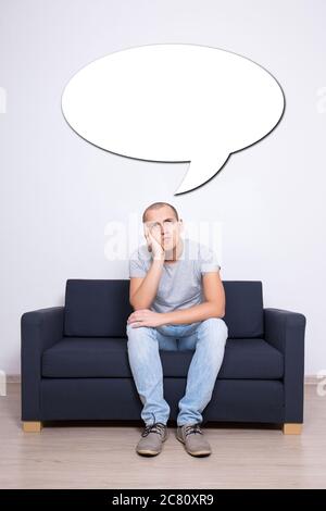 Idee Konzept - nachdenklicher Mann sitzt auf dem Sofa zu Hause und leere Blase Stockfoto