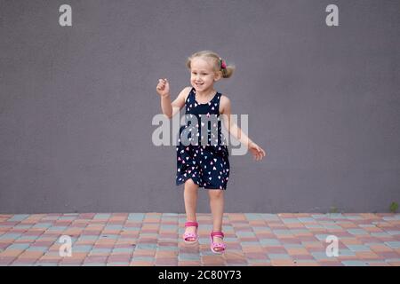 Porträt eines glücklichen liitle blonde Mädchen Nahaufnahme. 3 Yaers kaukasischen Todler Mädchen lächeln im Freien zu Fuß. Steinwand Hintergrund mit Kopierraum. Kind Stockfoto