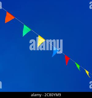 Farbenfrohe dreieckige Flaggen zieren den hellblauen Himmel bei einer festlichen Veranstaltung im Freien in einer lebhaften Atmosphäre Stockfoto