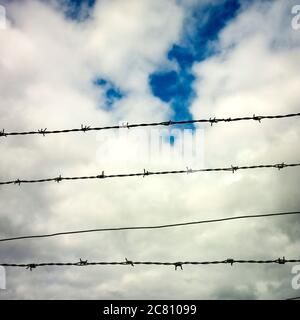 Stacheldrahtzaun vor einem bewölkten Himmel mit Anklängen von Blau, das während der Tageslichtstunden durchblickt Stockfoto