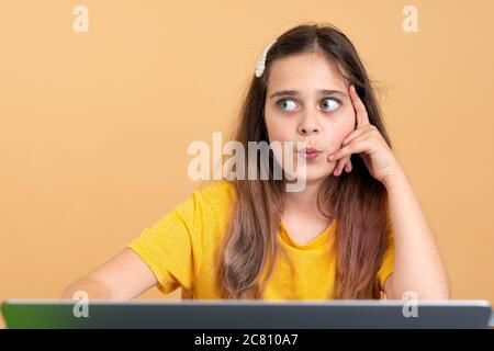 Ein nachdenkliches Kind, das auf der linken Seite auf dem Schreibtisch neben dem Laptop sitzt Stockfoto