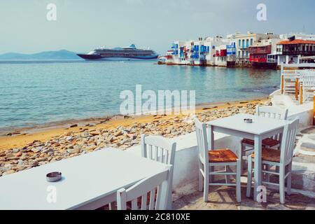 Cafe-Tisch und Kreuzfahrtschiff in der Ägäis. Chora, Mykonos Island, Griechenland Stockfoto
