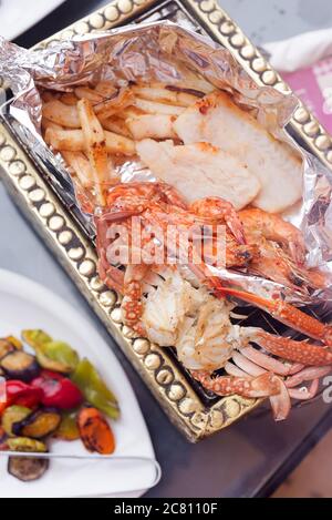 Nahaufnahme des Abendessens von frisch zubereiteten Fisch- und Meeresfrüchten aus dem Grill, natürlich gefischten Krabben, Tintenfischen und Garnelen auf einem Coopper Tablett mit gegrilltem Gemüse. Gesundheit Stockfoto