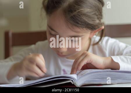 Grundschülerin macht ihre Hausaufgaben. Sie macht ihre eigenen Hausaufgaben allein zu Hause, weil die Schulen wegen der Corona pandemi geschlossen sind Stockfoto
