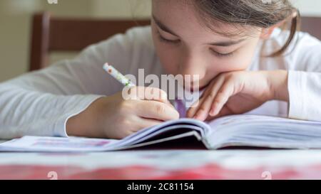 Grundschülerin macht ihre Hausaufgaben. Sie macht ihre eigenen Hausaufgaben allein zu Hause, weil die Schulen wegen der Corona pandemi geschlossen sind Stockfoto