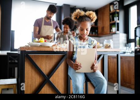 Cute African American Girl mit einem Tablet, während ihre Eltern Essen zubereiten in der Küche Stockfoto