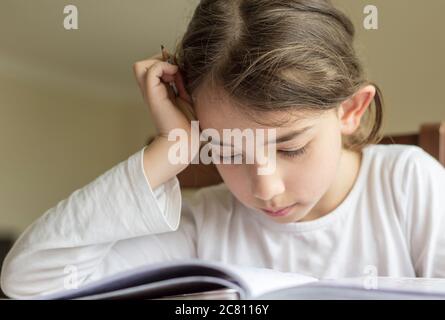 Grundschülerin macht ihre Hausaufgaben. Sie macht ihre eigenen Hausaufgaben allein zu Hause, weil die Schulen wegen der Corona pandemi geschlossen sind Stockfoto