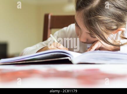 Grundschülerin macht ihre Hausaufgaben. Sie macht ihre eigenen Hausaufgaben allein zu Hause, weil die Schulen wegen der Corona pandemi geschlossen sind Stockfoto