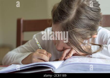 Grundschülerin macht ihre Hausaufgaben. Sie macht ihre eigenen Hausaufgaben allein zu Hause, weil die Schulen wegen der Corona pandemi geschlossen sind Stockfoto