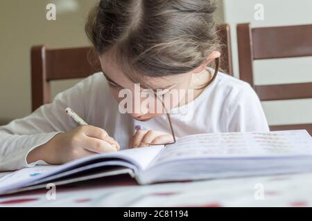 Grundschülerin macht ihre Hausaufgaben. Sie macht ihre eigenen Hausaufgaben allein zu Hause, weil die Schulen wegen der Corona pandemi geschlossen sind Stockfoto