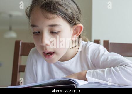 Grundschülerin macht ihre Hausaufgaben. Sie macht ihre eigenen Hausaufgaben allein zu Hause, weil die Schulen wegen der Corona pandemi geschlossen sind Stockfoto