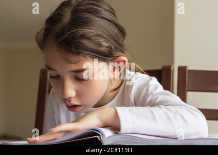 Grundschülerin macht ihre Hausaufgaben. Sie macht ihre eigenen Hausaufgaben allein zu Hause, weil die Schulen wegen der Corona pandemi geschlossen sind Stockfoto