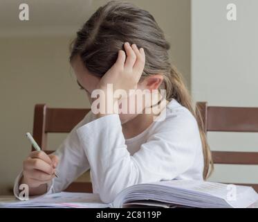 Grundschülerin macht ihre Hausaufgaben. Sie macht ihre eigenen Hausaufgaben allein zu Hause, weil die Schulen wegen der Corona pandemi geschlossen sind Stockfoto