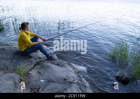 Fischerfrau sitzt auf Stein in der Nähe des Sees Stockfoto
