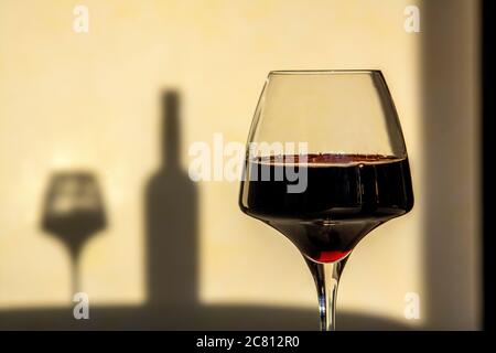 Ein Glas Rotwein auf einem Tisch, das den Schatten einer Weinflasche vor einem hellen Hintergrund wirft Stockfoto