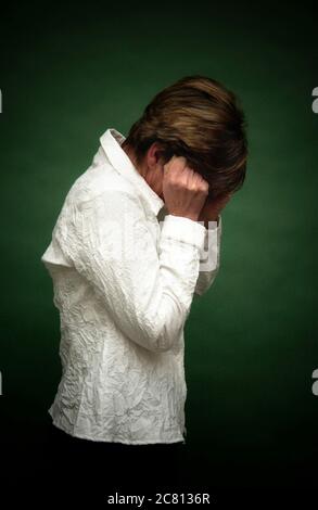 Frau mit verstörtem Ausdruck, die ihr Gesicht in einem schwach beleuchteten Raum während eines emotionalen Moments bedeckt Stockfoto