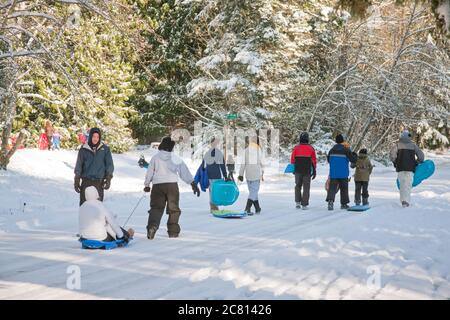 Gruppe von Jugendlichen, die mit Schlitten auf schneebedeckter Straße in Issaquah, Washington, USA, wandern Stockfoto