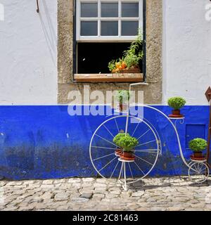 Charmante mittelalterliche Straße der Altstadt Obidos in Portugal. Vintage Fahrrad mit grünen Pflanzen und Korb mit hellen Orangen in der offenen gewinnen dekoriert Stockfoto