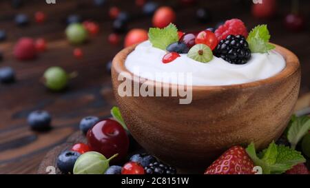 Schüssel Joghurt mit Waldbeeren auf dunklem Holzhintergrund Stockfoto