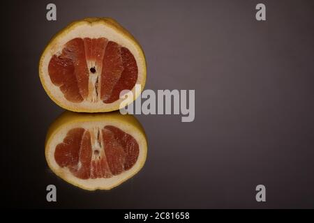 Halb transparente Grapefruitscheibe auf einem Hintergrund mit Spiegelung. Stockfoto