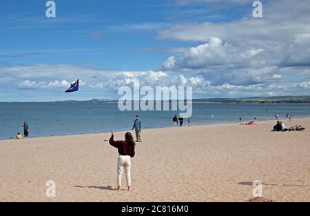 Portobello, Edinburgh, Schottland, Großbritannien. 20. Juli 2020. Diese junge Frau hat Spaß fliegen ihren Drachen über einen sehr ruhigen Strand für die Mitte Juli. Wetter Sonne und Cumulus Wolken mit windigen Bedingungen. Wind West 23 km/h Böen 37 km/h Temperatur 17 Grad. Stockfoto