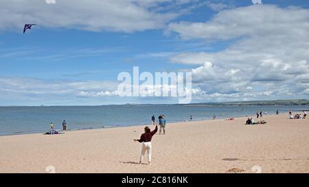 Portobello, Edinburgh, Schottland, Großbritannien. 20. Juli 2020. Diese junge Frau hat Spaß fliegen ihren Drachen über einen sehr ruhigen Strand für die Mitte Juli. Wetter Sonne und Cumulus Wolken mit windigen Bedingungen. Wind West 23 km/h Böen 37 km/h Temperatur 17 Grad. Stockfoto