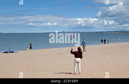 Portobello, Edinburgh, Schottland, Großbritannien. 20. Juli 2020. Diese junge Frau hat Spaß fliegen ihren Drachen über einen sehr ruhigen Strand für die Mitte Juli. Wetter Sonne und Cumulus Wolken mit windigen Bedingungen. Wind West 23 km/h Böen 37 km/h Temperatur 17 Grad. Stockfoto