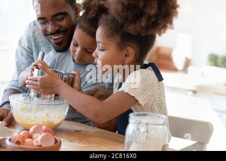 Fröhlicher Biracial Vater und kleine Kinder machen Teig für Gebäck Stockfoto