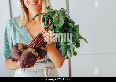 Junge Frau in der Mitte hält rote Beete mit grünen Blättern und lächelt Stockfoto