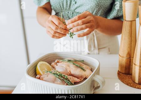 Nahaufnahme der weiblichen Hände, die Thymianwürze zu roh hinzufügen Hähnchen Stockfoto