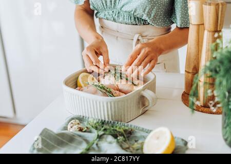 Weibliche Hände hinzufügen aromatische Kräuter zu Huhn zum Braten Stockfoto