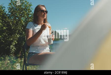 Frau isst Instant Nudeln neben dem Zelt am See. Stockfoto