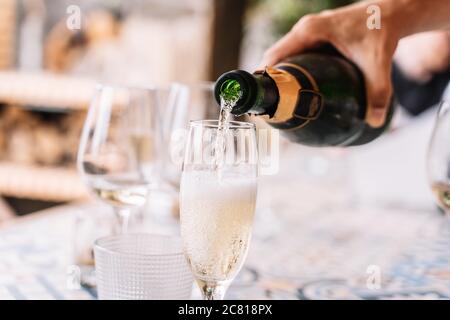 Hand einer Person, die Champagner auf ein paar Gläser vom Tisch außerhalb des Gartens setzt Stockfoto