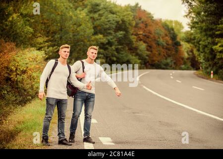 Männer Rucksäcke, die auf der Straße laufen, Zwillinge, die auf der Straße spazieren gehen. Abenteuer und Entdeckung. Mann mit Rucksackhitchwandern auf der Straße. Sommerurlaub. Touristenreisende fahren mit Auto. Budget-Reisende. Stockfoto