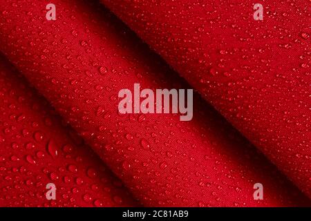 Abstrakter Hintergrund aus hydrophobem Stoff. Wassertropfen auf knittertem rotem Stoff. Stockfoto