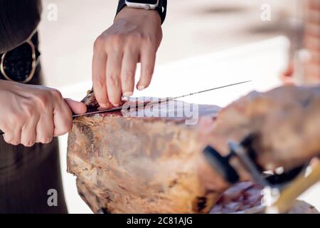 Frau schneidet iberischen Schweineschinken mit einem Schinkenhalter und Messer Stockfoto