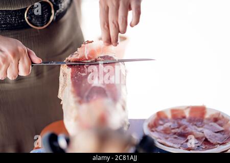 Frau schneidet iberischen Schweineschinken mit einem Schinkenhalter und Messer Stockfoto