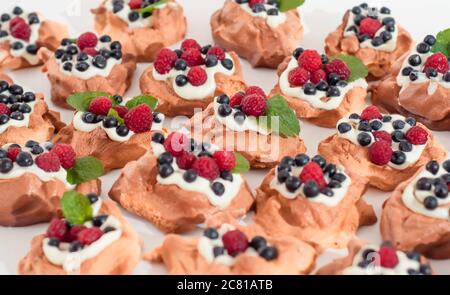 Mini Pavlova Meringue Nester mit Beeren und Minze auf isoliert auf weiß Stockfoto