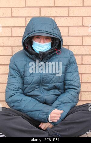 Negatives Leben Ereignis neu obdachlos mit verquetschtes Auge trägt eine Maske auf dem Boden sitzen betteln um Geld Stockfoto