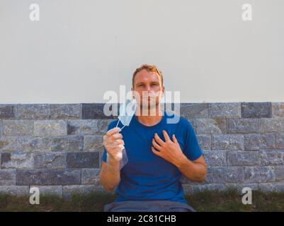 Portrait von Kerl mit einer medizinischen Maske. Draußen zu Fuß im Garten in der Nähe von modernen Sommerhaus. Er will atmen, auf das Ende der Quarantäne warten Stockfoto